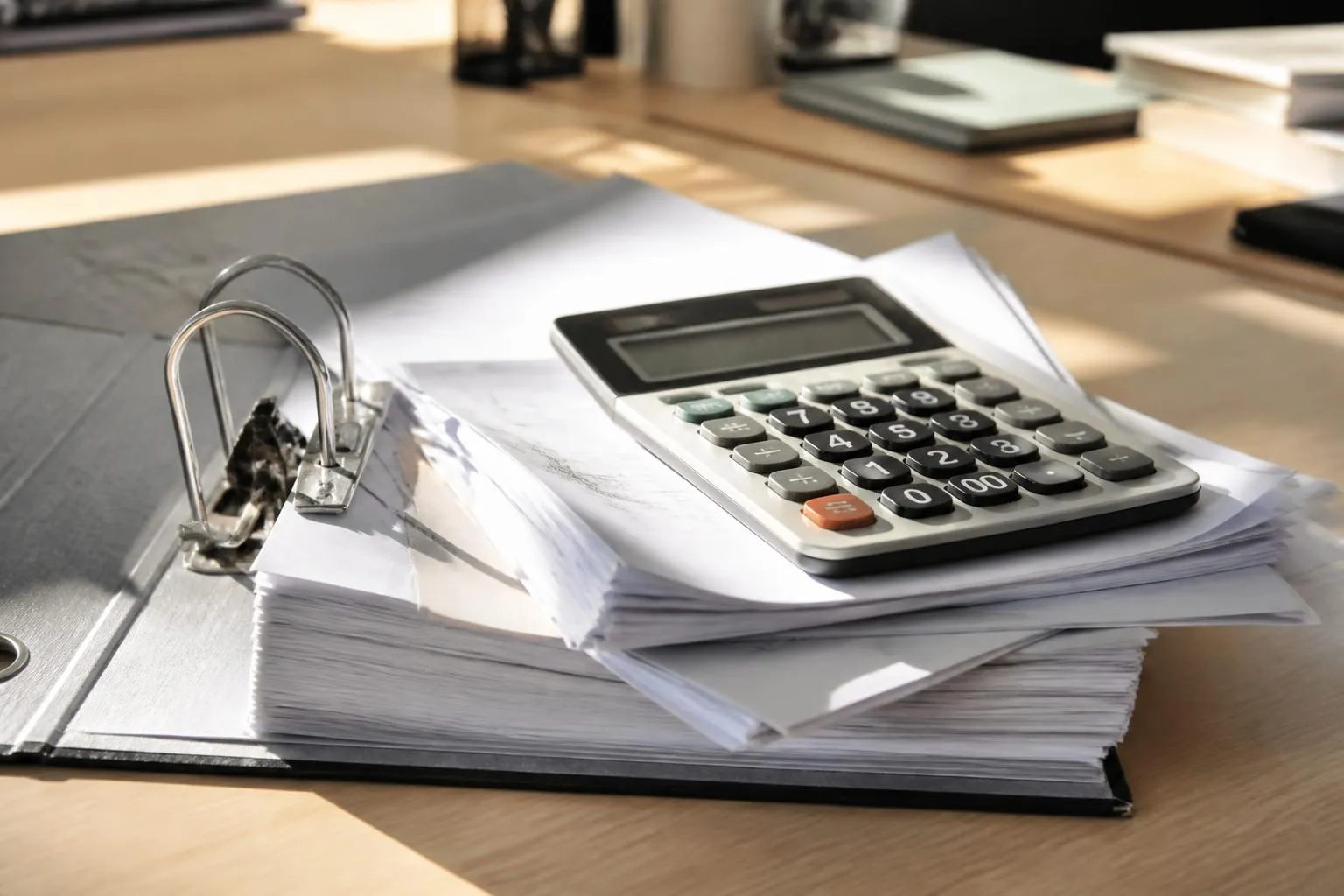 Un classeur de factures ouvert sur un bureau, à côté d'une calculatrice de bureau et d'un relevé Urssaf.