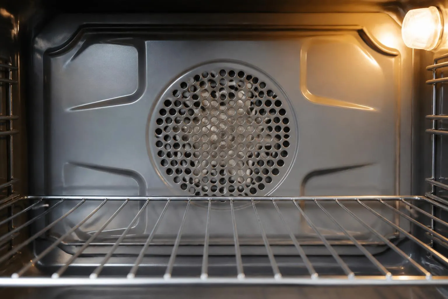 Paroi du fond d'un four vide, avec sa grille circulaire de ventilateur au centre et une grille métallique glissée au niveau du milieu.